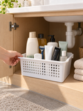 Before and after bathroom under-sink cabinet - left chaotic pile of 30+ loose toiletries, right three white ventilated baskets organized by category
